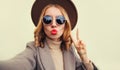 Fashionable portrait of stylish young woman stretching hand for taking selfie with phone blowing her lips with red lipstick Royalty Free Stock Photo