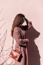 Fashionable pretty luxurious young woman model in stylish coat with handbag in sunglasses posing near vintage pink wall on sunny