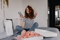 Fashionable red-haired girl sitting on bed with phone. Pleasant caucasian woman spending time at ho Royalty Free Stock Photo