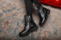 Fashionable seasonal leather black lace-up boots close-up. Stylish young woman is sitting on a red sofa in trendy shoes in vintage