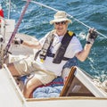 An elderly seafarer manages a sailing boat on a sunny summer day.