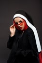 Fashionable sexy demoniac nun with red eyes posing in black suit, red sunglasses and scarf