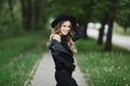 Fashionable and sexy young model woman in a black leather jacket and in trendy jeans adjusting her stylish black hat and Royalty Free Stock Photo