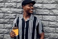 Fashionable smiling african american man in hat, man outdoors with takeaway coffee cup, over gray wall background Royalty Free Stock Photo