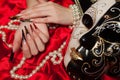 Fashionable stilettos nails design with Venetian buffoon mask, beads on red silk