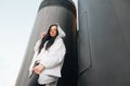 Fashionable street portrait of a woman in a white jacket and casual clothing poses on the urban location, looking into the camera