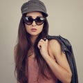 Fashionable style female model in fashion sunglasses posing holding the hand black leather jacket on blue background. Summer