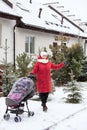 Fashionable stylish young mother stands with her baby stroller in courtyard at winter. Showing street covered with snow Royalty Free Stock Photo