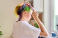 Fashionable teen girl with trendy rainbow dyed hair combing hair at home