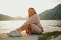 Fashionable teenage girl in a long dress and sneakers. Cute long-haired girl resting on the beach near mountains and ocean