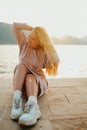 Fashionable teenage girl in a long dress and sneakers. Cute long-haired girl resting on the beach near mountains and ocean Royalty Free Stock Photo