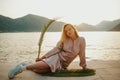 Fashionable teenage girl in a long dress and sneakers. Cute long-haired girl resting on the beach near mountains and ocean