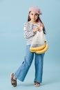 Fashionable tween girl in french beret holding net bag with bananas. Royalty Free Stock Photo