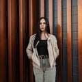 Fashionable urban young woman fashion model in youth leather beige jacket in trendy black t-shirt in jeans rests near metal Royalty Free Stock Photo