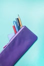 Fashionable violet pencil case with multicolored felt-tip pens, pencils and pens on green background. Royalty Free Stock Photo