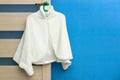 Fashionable white female coat hanging on door handle on blue wall background