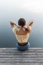 Fashionable woman with blouse top. in blue jeans straightens her hair and sits on a wooden pier near the water Royalty Free Stock Photo