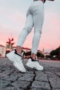 Fashionable woman in denim white jeans and trendy sneakers walking in the city at pink sunset