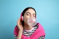 Fashionable woman with headphones blowing bubblegum on light blue background Royalty Free Stock Photo