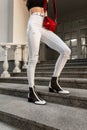 Fashionable woman in jeans in black and white shoes with a red handbag posing on the steps in the city