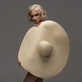 Fashionable woman posing with a large wide-brimmed hat. Gray background