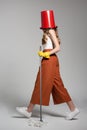 Fashionable woman with a red bucket on her head holding a mop. Royalty Free Stock Photo