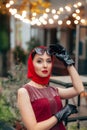 A fashionable woman with sunglasses, in a red dress stands on the street of the evening city with illumination Royalty Free Stock Photo