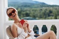 fashionable woman in sunglasses sits on the balcony and uses the phone Perfect sunny morning Royalty Free Stock Photo