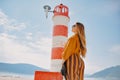 Fashionable woman on vacation against the backdrop of the sea, mountains and a lighthouse. Summer, sunny day, walk along the beach