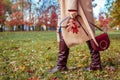 Fashionable woman wearing stylish clothes shoes and accessories walking in fall park. Autumn leather boots and purse