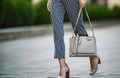 Fashionable woman wears high-heels shoes, blue cotton pants with white stripes and hold grey bag outdoors. Generative AI