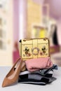 A fashionable yellow luxury handbag on a stack of folded women`s clothes and a single elegant shoe on the table over abstract Royalty Free Stock Photo