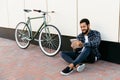 Happy bearded man using a tablet while sitting on the ground near the bike Royalty Free Stock Photo