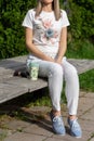 Girl in striped pants and blue shoes sitting on a wooden bench next to a cup of coffee and sunglasses in the park on spring sunny Royalty Free Stock Photo