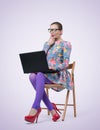 Fashionable young businesswoman in dress and glasses sitting on wooden chair with laptop Royalty Free Stock Photo