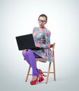 Fashionable young businesswoman in dress and glasses sitting on wooden chair with laptop Royalty Free Stock Photo