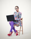 Fashionable young businesswoman in dress and glasses sitting on wooden chair with laptop Royalty Free Stock Photo