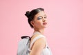 Fashionable young girl wears holding backpack, posing on pink background