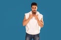 Fashionable young handsome man posing in white tank top with hood on blue studio background. Bearded guy looking at the camera Royalty Free Stock Photo