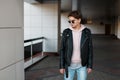 Fashionable young hipster man in black sunglasses in stylish black jacket in pink sweatshirt in trendy jeans in a gray t-shirt Royalty Free Stock Photo