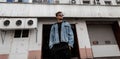 Fashionable young hipster man in youth stylish clothes in trendy sunglasses stands near a vintage white building in the city on a