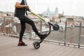 Fashionable young man in a denim vest in a T-shirt in gray jeans in sneakers posing with an electric scooter on a summer terrace. Royalty Free Stock Photo