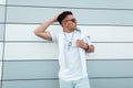 Fashionable young man fashion model in stylish summer clothes in trendy sunglasses posing in the city near a modern wall. Urban Royalty Free Stock Photo