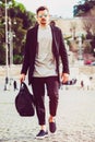Fashionable young man with holdall bag walking in the street in the city. Wearing sunglasses. Royalty Free Stock Photo