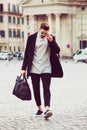 Fashionable young man walking in the street in the city. With sunglasses and a bag in his hand. Royalty Free Stock Photo