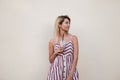 Fashionable young positive woman in a stylish pink striped sundress stands near a vintage wall with a tasty milkshake in hands.