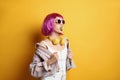 Fashionable young woman in colorful wig with headphones blowing bubblegum on yellow background, space for text Royalty Free Stock Photo