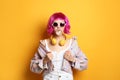 Fashionable young woman in colorful wig with headphones blowing bubblegum on yellow background Royalty Free Stock Photo