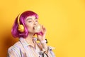 Fashionable young woman in colorful wig with headphones blowing bubblegum on yellow background, space for text Royalty Free Stock Photo