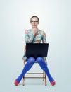 Fashionable young woman in dress and glasses sitting on chair with a laptop Royalty Free Stock Photo